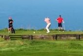 three people playing golf overlooking the sea